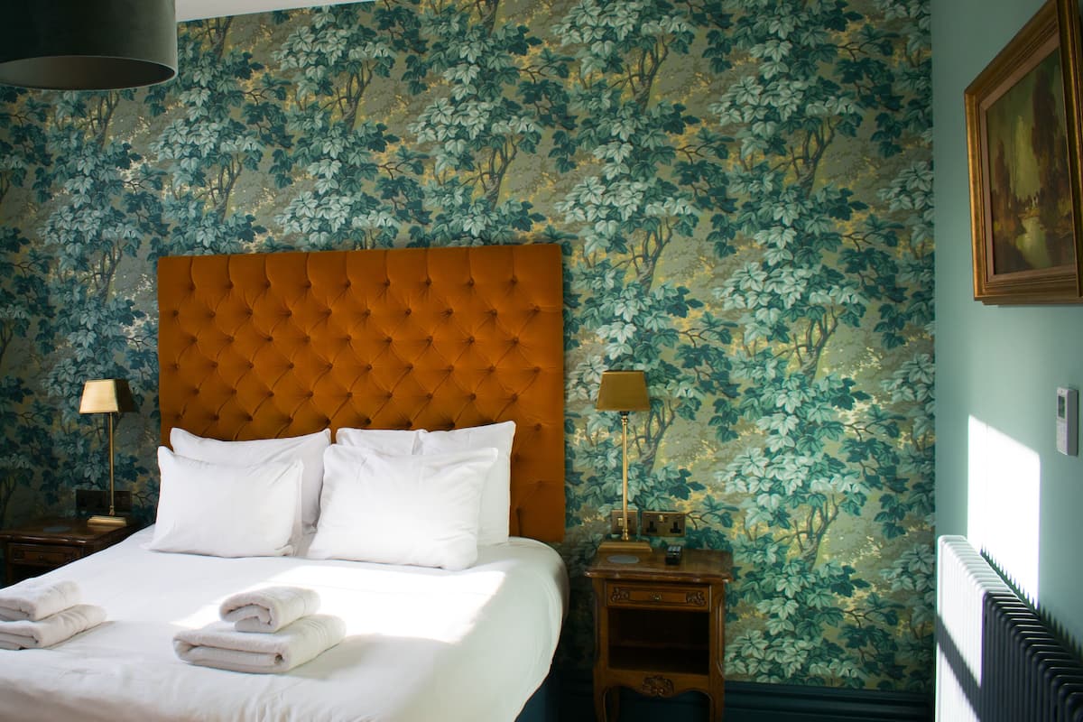 A hotel room with a large bed, two bedside tables, a window with curtains, and floral wallpaper.