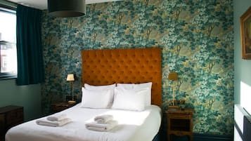 A hotel room with a large bed, two bedside tables, a window with curtains, and floral wallpaper.