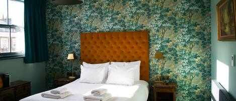 A hotel room with a large bed, two bedside tables, a window with curtains, and floral wallpaper.