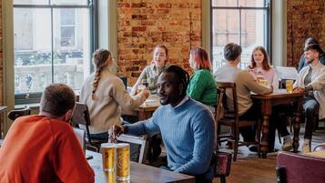 A group of people seated at tables in a restaurant with brick walls and large windows.