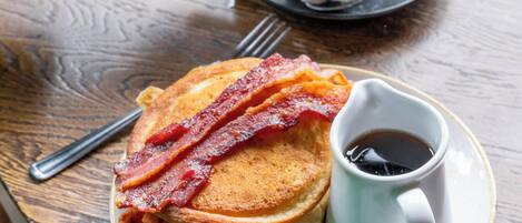 En frukostuppsättning med pannkakor, bacon, en kopp kaffe och en tekanna som häller upp te.