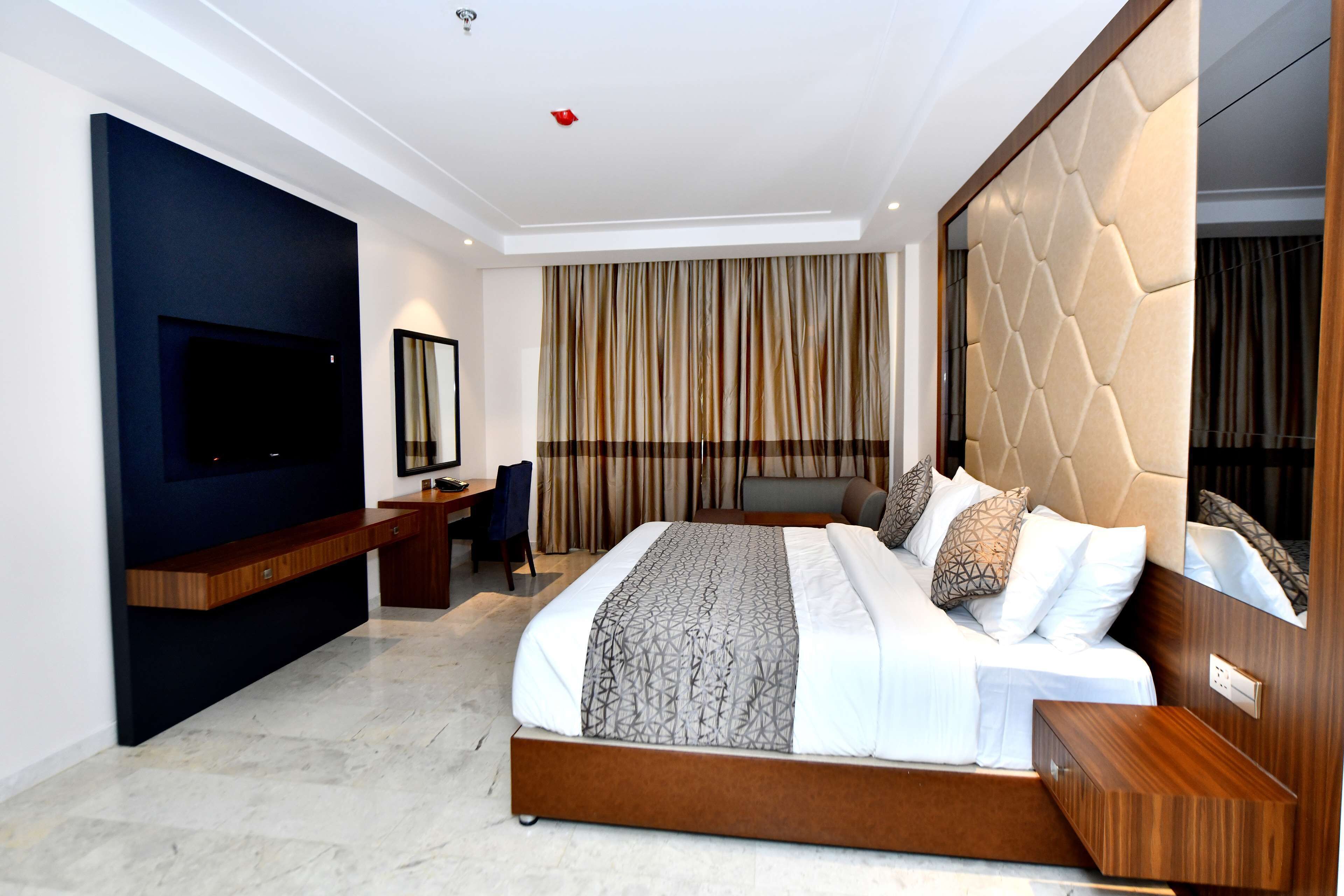 Une chambre d’hôtel moderne dotée d’un grand lit, d’un téléviseur à écran plat, d’un bureau et d’une grande fenêtre avec des rideaux.