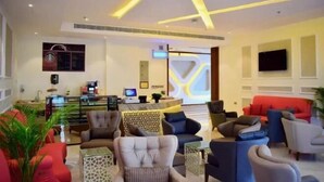 Eine moderne Hotelhalle mit einer Rezeption, einer Sitzecke mit Sofas und Sesseln sowie einem dekorativen Deckenmuster.