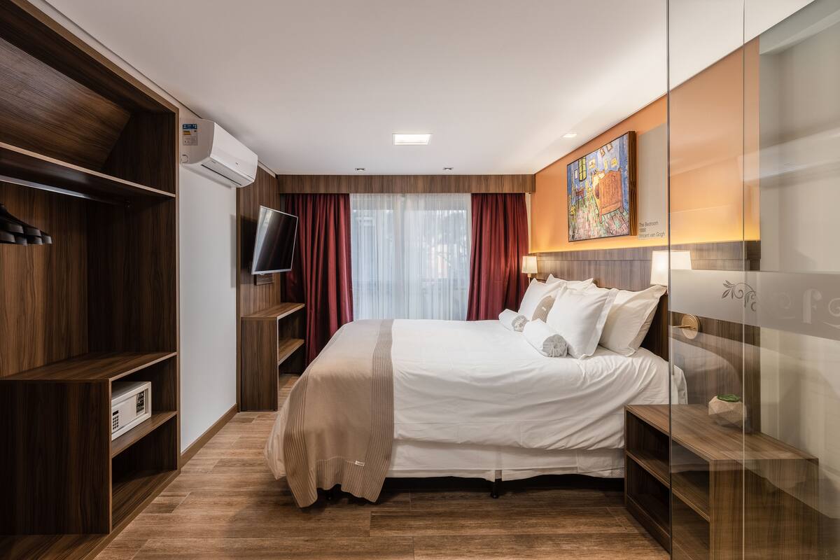 A modern hotel room with a large bed, wooden shelving, a flat-screen TV, and a painting on the wall.