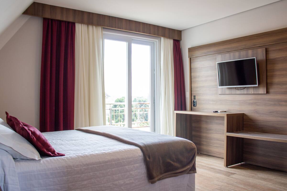 A bedroom with a bed, a TV mounted on the wall, and a balcony with curtains.