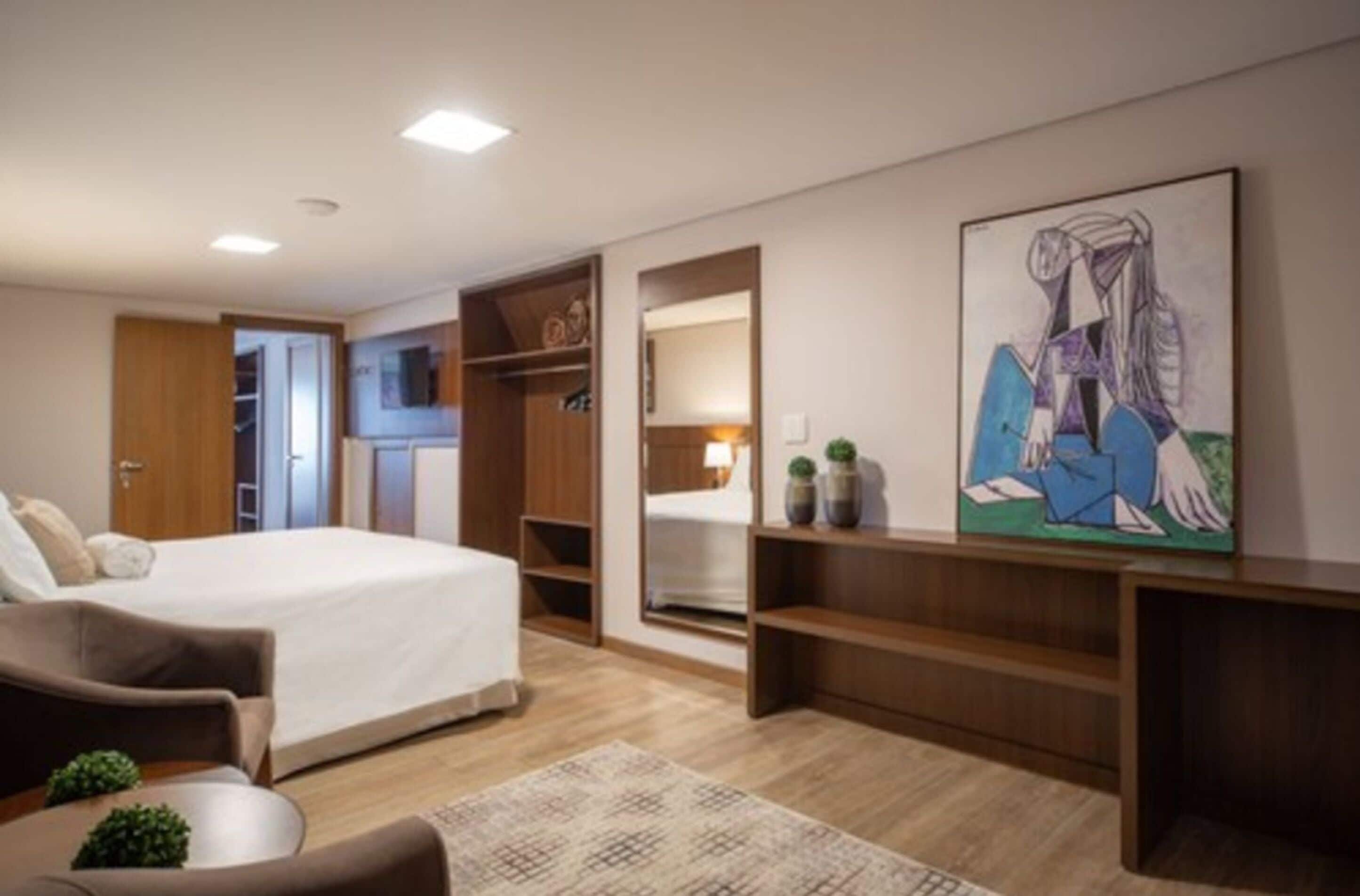 Una habitación de hotel moderna con cama, zona de estar, escritorio y un cuadro abstracto grande en la pared.