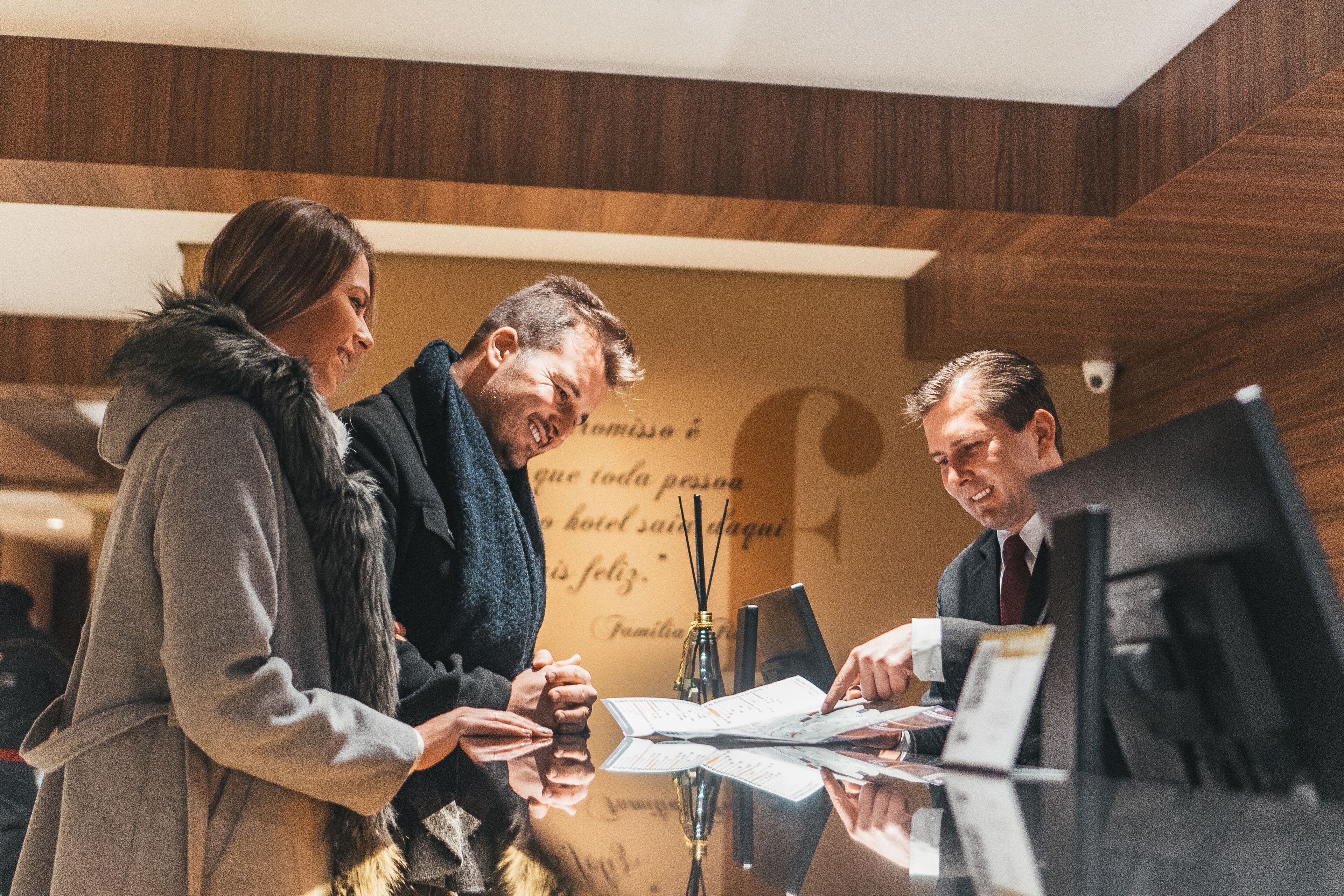Tres personas en la recepción de un hotel con detalles de madera y un letrero con texto.