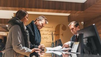 Tres personas en la recepción de un hotel con detalles de madera y un letrero con texto.