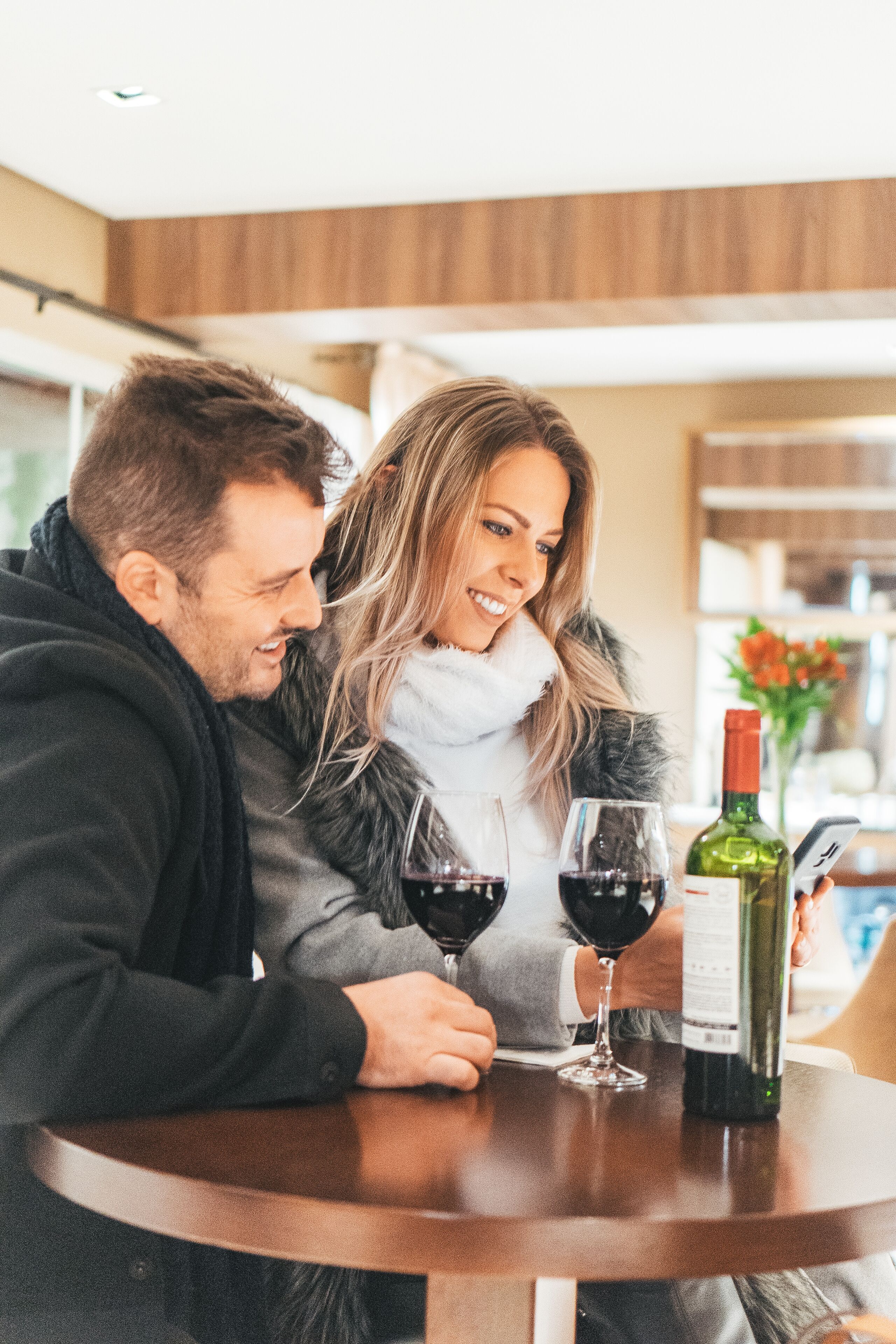 A couple sitting at a round table with two wine glasses and a bottle of wine.