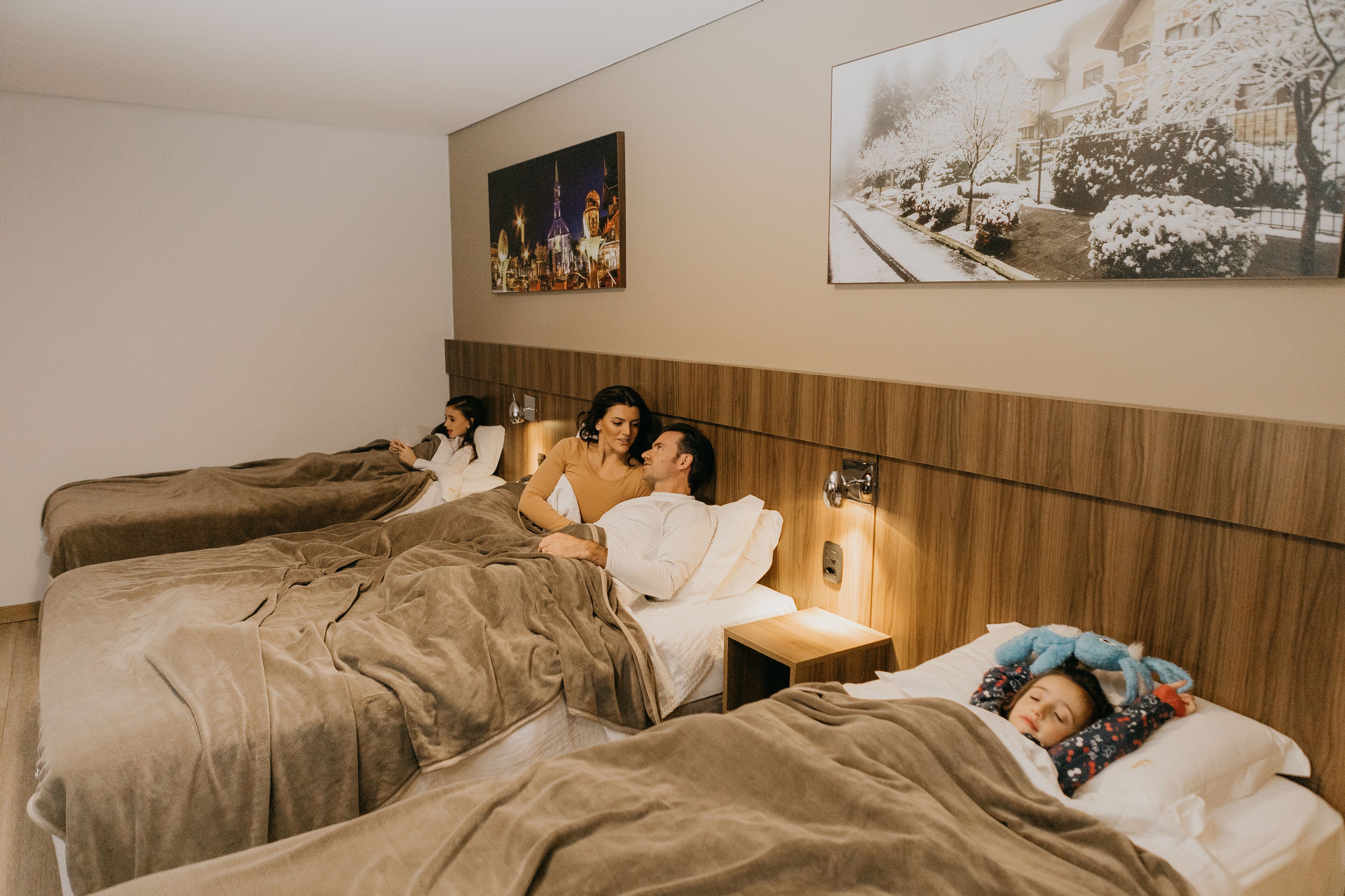 A hotel room with four beds arranged in a row, wooden headboard, and two wall-mounted paintings.