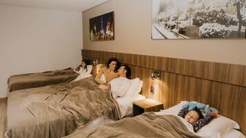 A hotel room with four beds arranged in a row, wooden headboard, and two wall-mounted paintings.