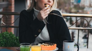 Una persona sentada a una mesa con diferentes alimentos para el desayuno, incluyendo huevos, bollería y una taza de café.