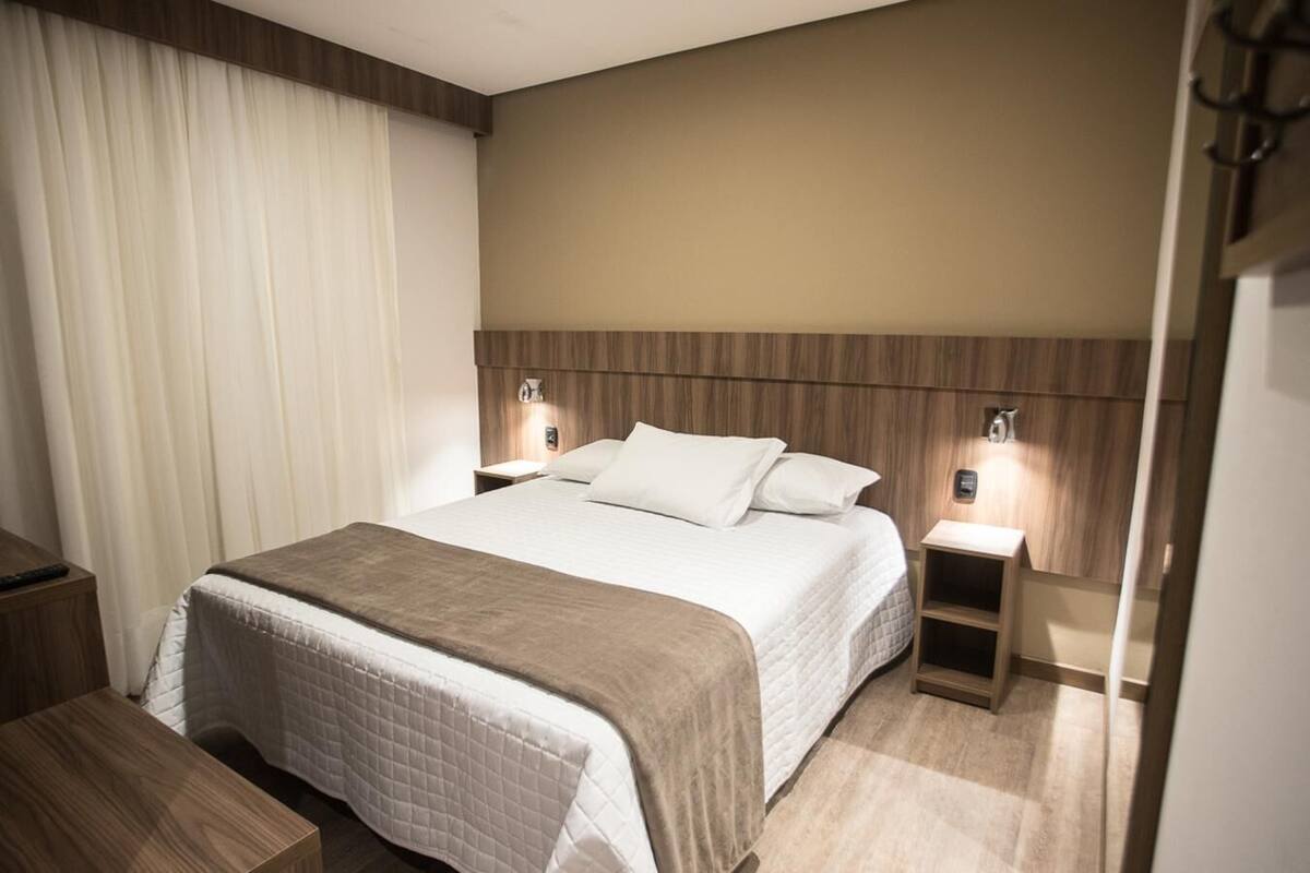 A hotel room with a bed, bedside tables, a nightstand, and a wooden headboard.