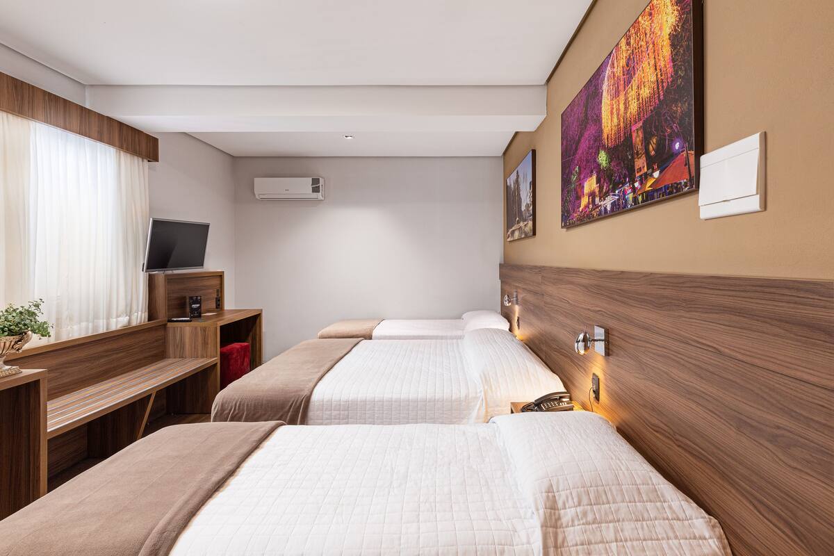 A hotel room with two beds, a desk, a television, and artwork on the wall.