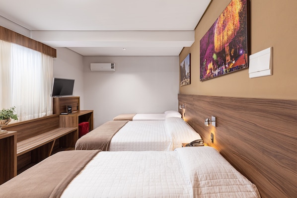 A hotel room with two beds, a desk, a television, and artwork on the wall.