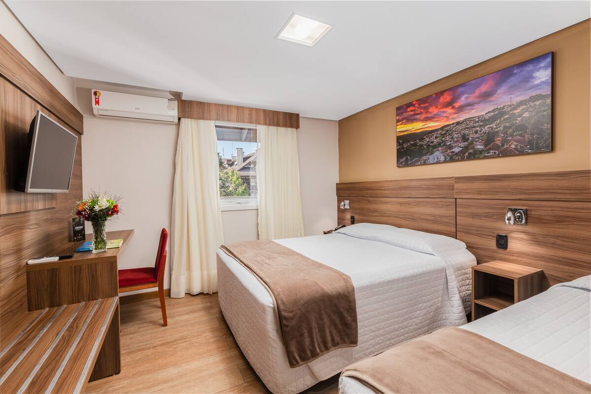 A hotel room with a bed, a desk with a chair, a TV, and a painting on the wall.