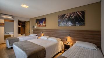 A hotel room with three beds, a wooden headboard, a nightstand with a phone, and two wall-mounted lamps.