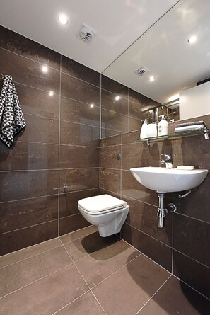 A modern bathroom with a white toilet, a large sink, and a glass shelf above the sink. - Yugo Explore - Amnis House (Cork)