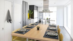 Una cocina moderna con una mesa de madera dispuesta para comer, equipada con hervidor, ollas y una planta en maceta.