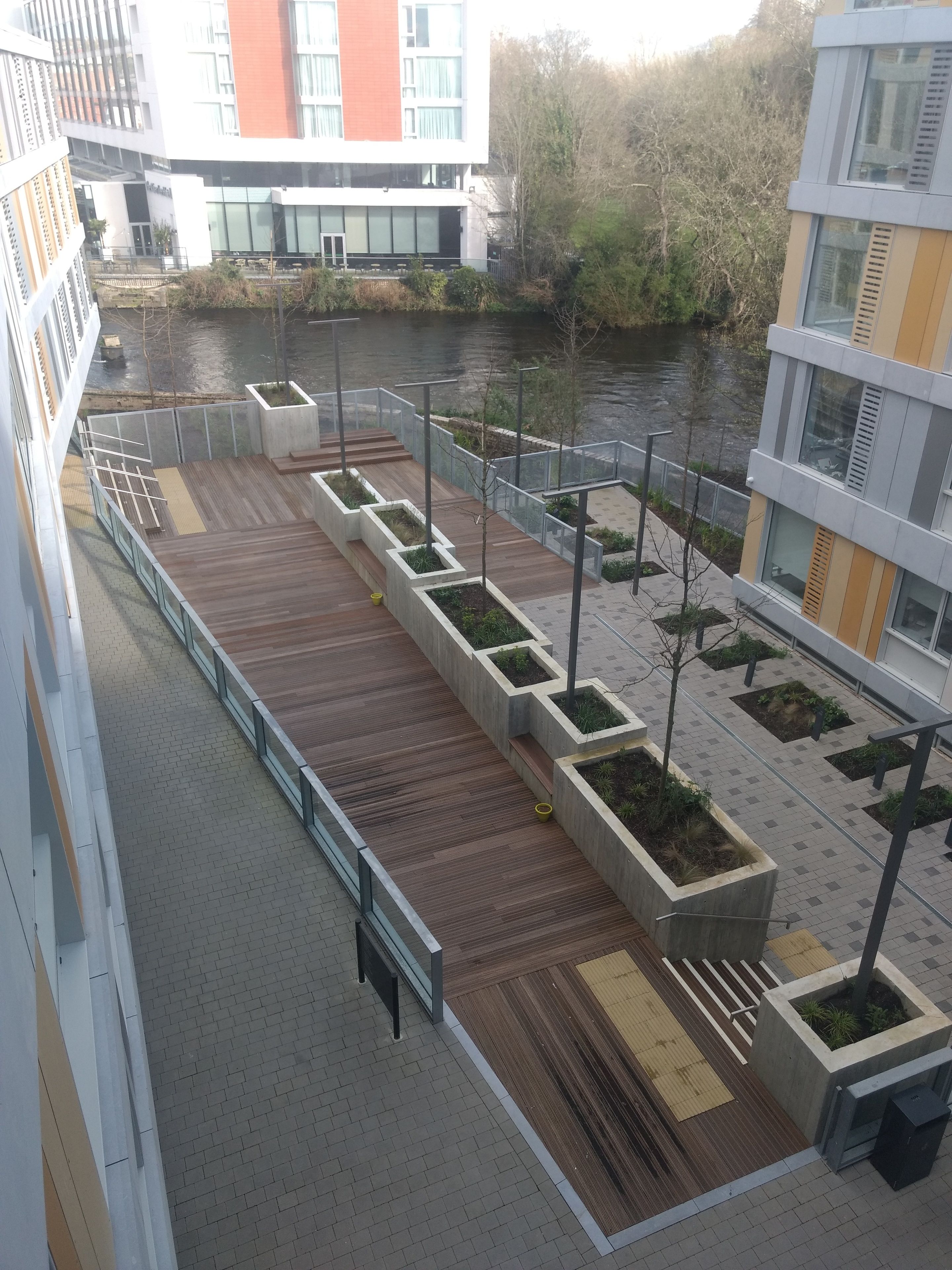 Un espacio exterior moderno con terraza de madera, jardineras y vistas a un río.