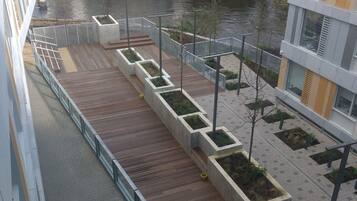 Un espacio exterior moderno con terraza de madera, jardineras y vistas a un río.