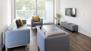 Una sala moderna con un sofá, un sillón y un televisor montado en la pared.