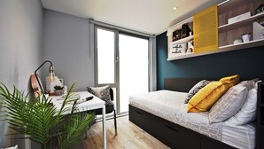 Un dormitorio moderno con cama, mesita de noche, lámpara y un gran ventanal.