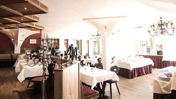 A restaurant with multiple tables and chairs, wooden beams on the ceiling, and a chandelier.