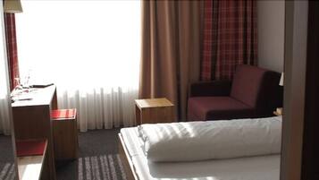 Quarto de hotel com cama, escrivaninha com cadeira, mesinha e poltrona vermelha.