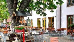 Un espace extérieur aménagé avec des tables et des chaises, situé sous un arbre et entouré de bâtiments dotés de grandes fenêtres.