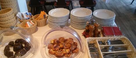 Montaje de bufé con diversos alimentos, incluyendo pasteles y salsas, dispuesto en una mesa con platos apilados y cestas.