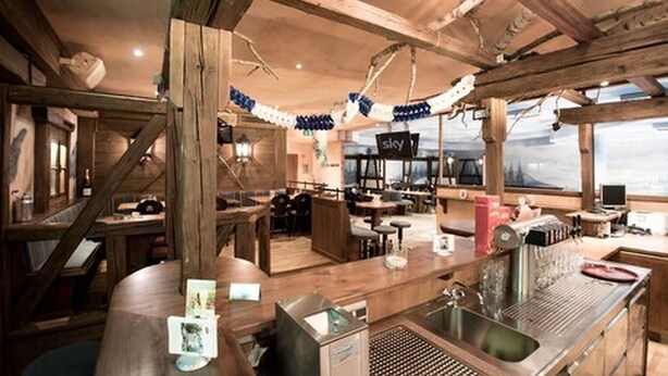 Un intérieur rustique avec des poutres en bois, un coin bar et une vue dégagée grâce à de grandes fenêtres.