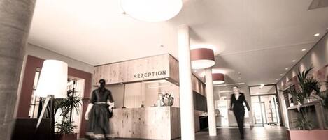 A reception area with a wooden reception desk labeled "RECEPTION" and a person walking in the background.