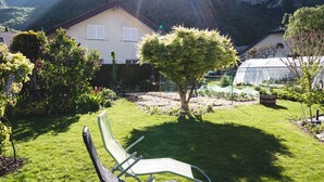 A grassy outdoor area with a metal chair, a small tree, and a house with a mountain in the background. - B&B Mon Rêve (Port-Valais)