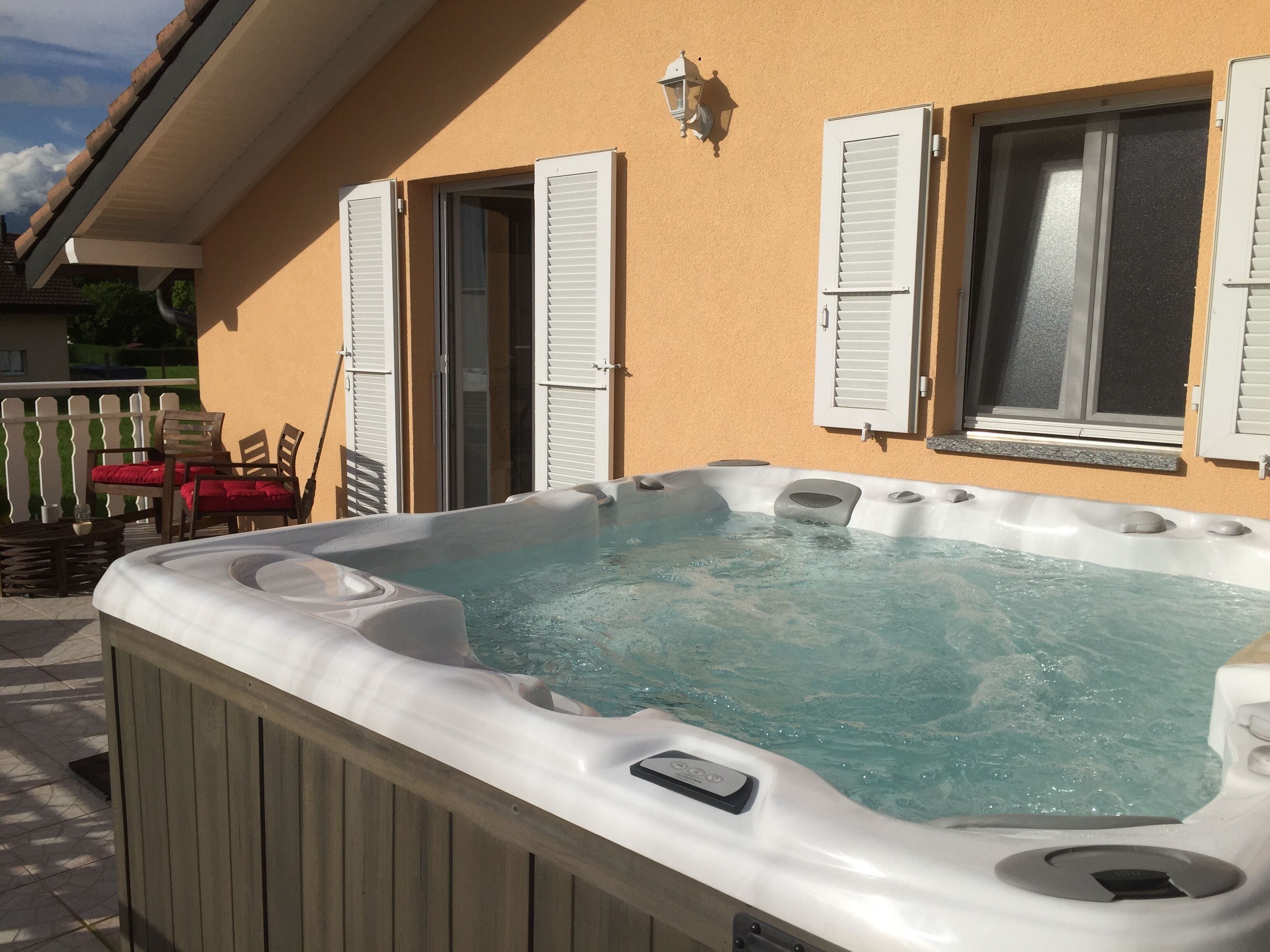Una vasca idromassaggio di fronte a una casa con un balcone, un recinto bianco e una sedia rossa.