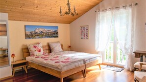 A bedroom with a wooden bed, a chandelier, a painting of mountains, and a view of greenery through a window. - B&B Mon Rêve (Port-Valais)