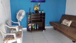 A living room with a blue wall, a TV mounted above a wooden cabinet, a brown sofa, and a white chair with a floral cushion. - Chacara So Alegria em Parnamirim (Parnamirim)