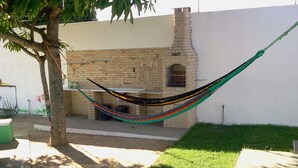 A hammock tied between two trees in a backyard with a brick patio and a stone wall. - Chacara So Alegria em Parnamirim (Parnamirim)