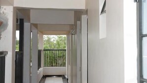A corridor with a tiled floor, white walls, and a balcony with a black railing.