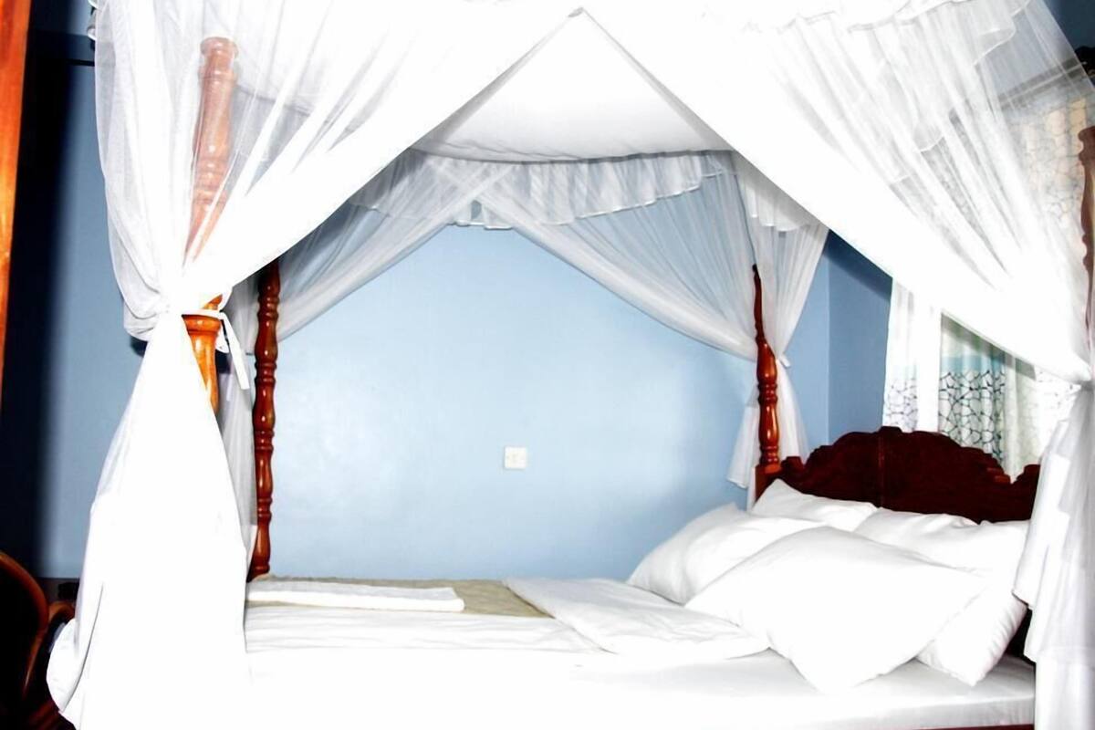 Uma cama com dossel, cabeceira de madeira e roupa de cama branca.