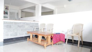 A room with a wooden table and two chairs, a tiled floor, and a white wall with a window.