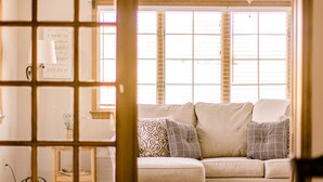 Ein Wohnzimmer mit einem beigefarbenen Sofa, gemusterten Kissen, Holzboden und Deckenventilator.