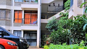 A multi-story residential building with balconies, a car parked in front, and lush greenery around. - Celestial Luxury Homestay (Syokimau)