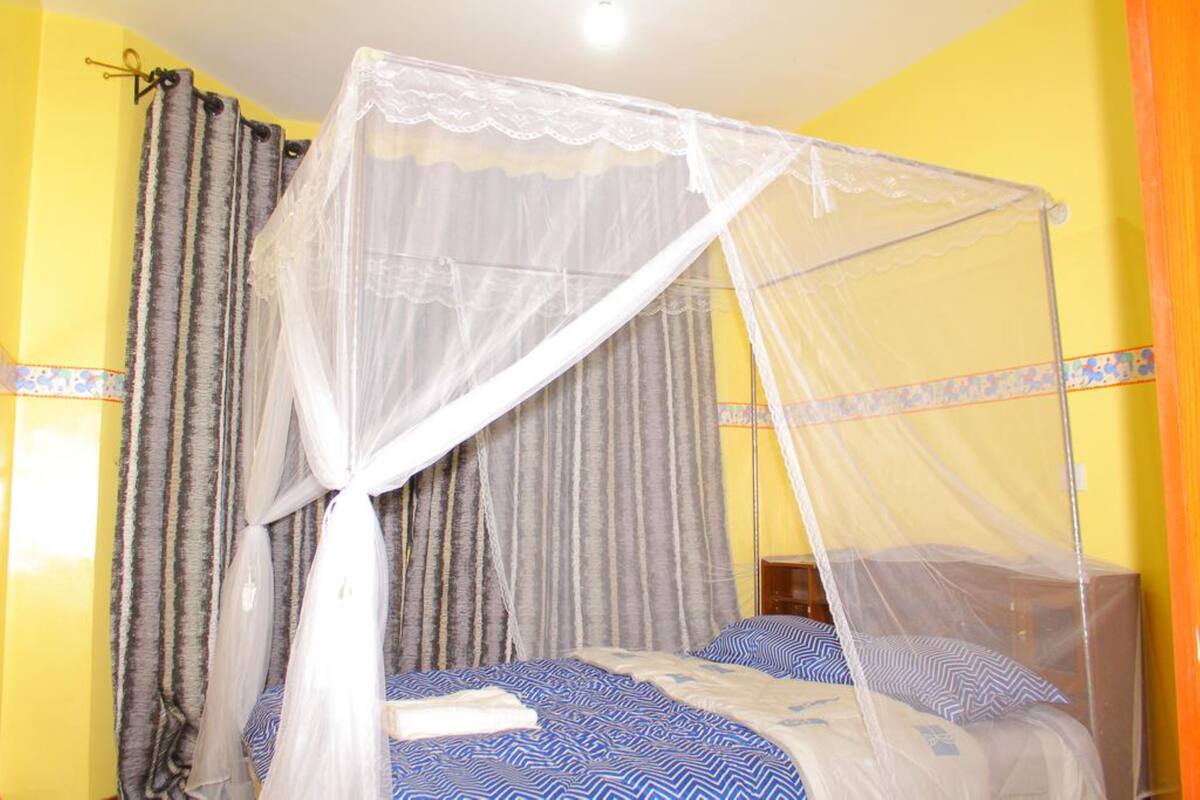 A bed with a white canopy and blue patterned bedding, curtains, and a wooden nightstand.