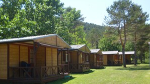 A row of wooden cabins with balconies, set in a grassy area with trees in the background. - Camping Pirinenc (Campdevanol)