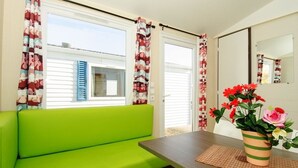 A bright room with a green sofa, a wooden table, and a potted plant with flowers. - Camping Pirinenc (Campdevanol)