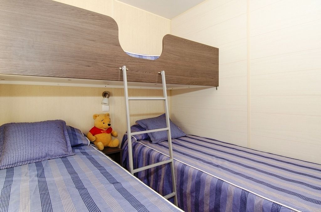 A dormitory room with bunk beds, a ladder, and a teddy bear on one bed.