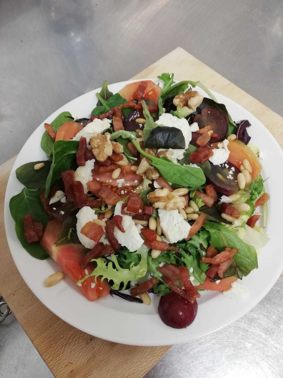 A plate of mixed greens salad with tomatoes, nuts, and cheese.