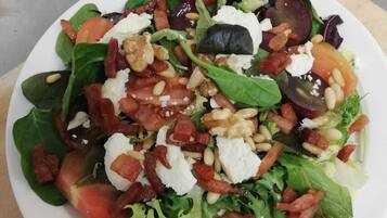 A plate of mixed greens salad with tomatoes, nuts, and cheese.