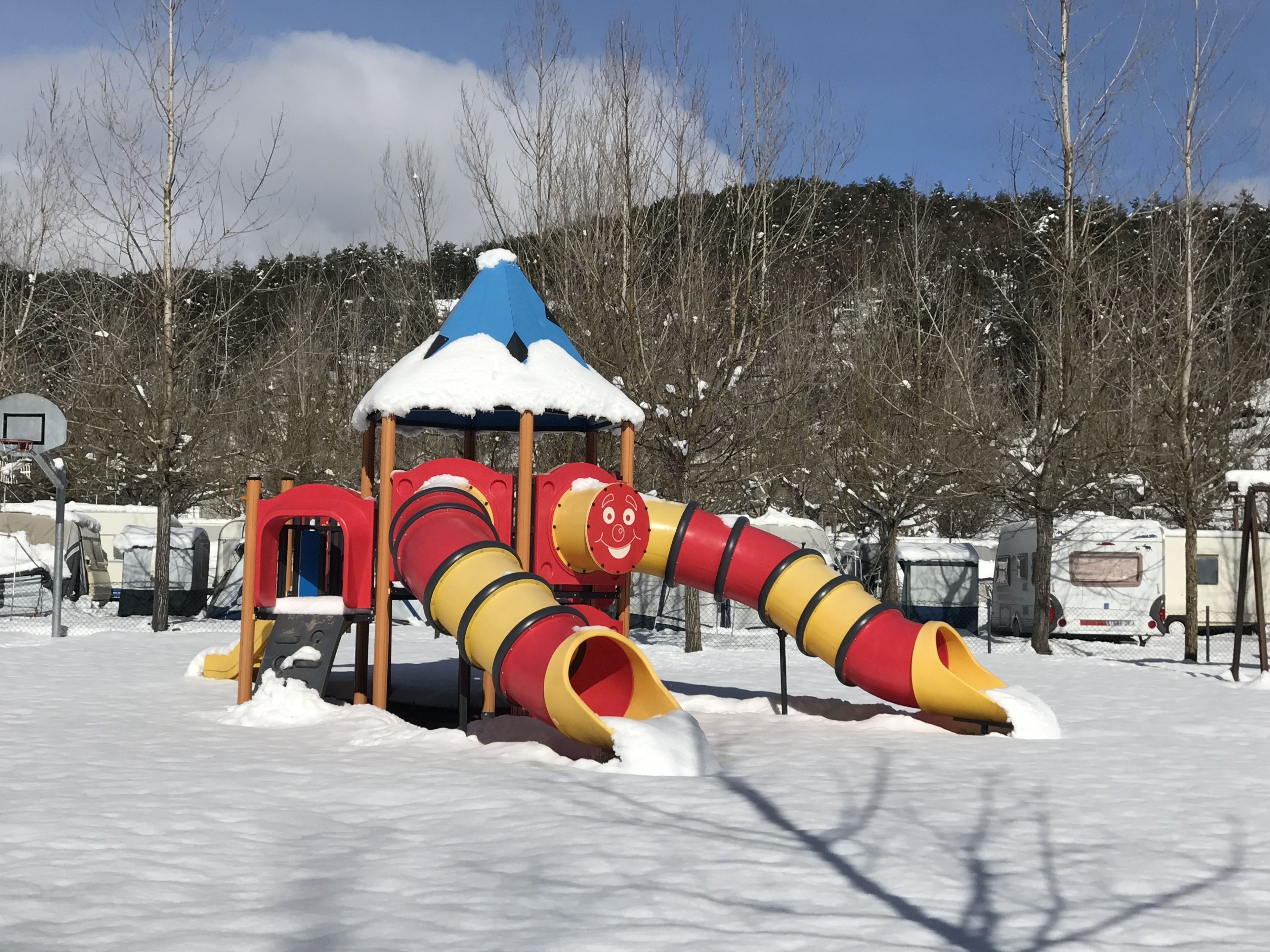 Une aire de jeux recouverte de neige, avec un toboggan et une structure d’escalade.